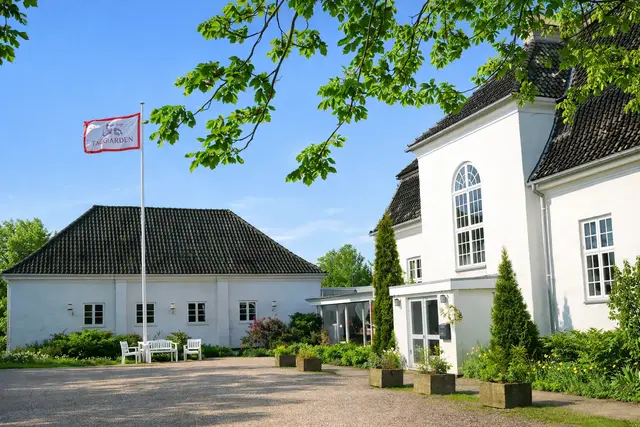 TaxGården, hvid patriciervilla i Bagsværd med flag og grønne omgivelser